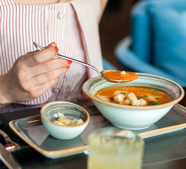 Close-up of a woman savoring tomato soup with croutons in an indoor setting.