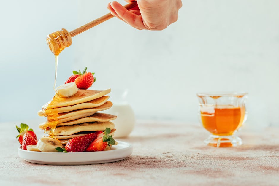Stack of pancakes with honey, banana, and strawberries, creating a perfect brunch scene.