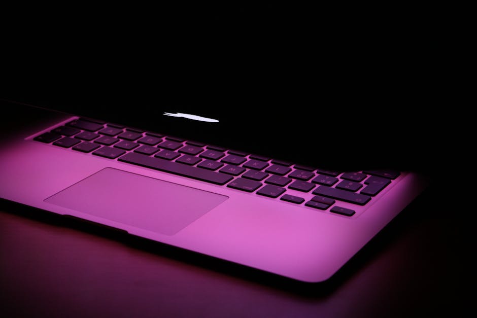 A stylish laptop partially closed, illuminated by a pink light, highlighting its modern design.