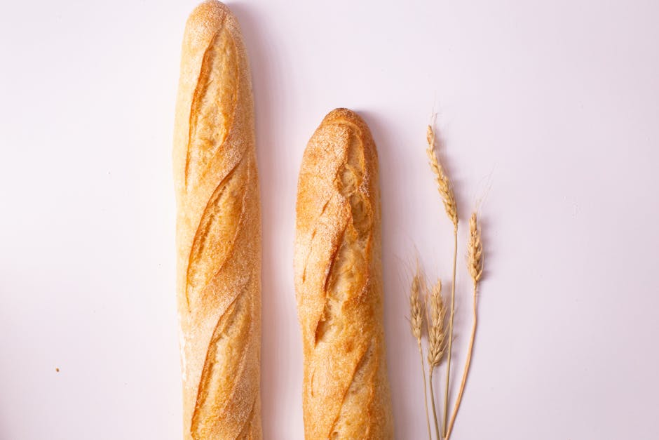 Pair of fresh baguettes on a white background with wheat stalks for a rustic look.