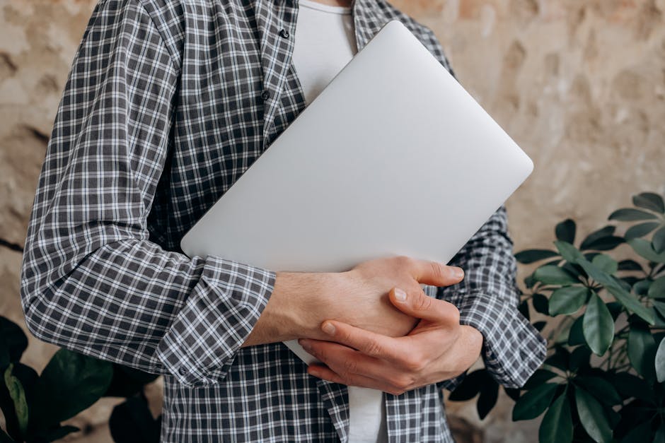 Close-up of a young adult casually holding a laptop indoors, showcasing modern freelance lifestyle.