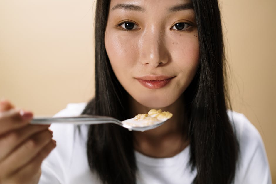 Portrait of an Asian woman holding a spoonful of cereal indoors, capturing a candid breakfast moment.