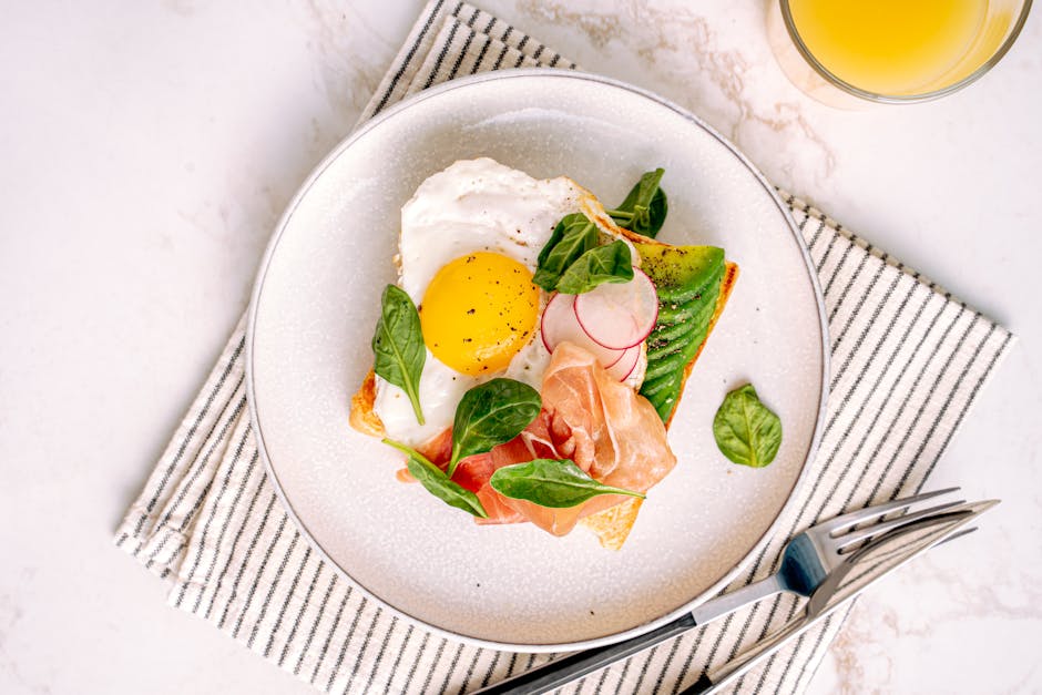 A mouth-watering breakfast toast featuring a fried egg, avocado, and prosciutto on a white plate.