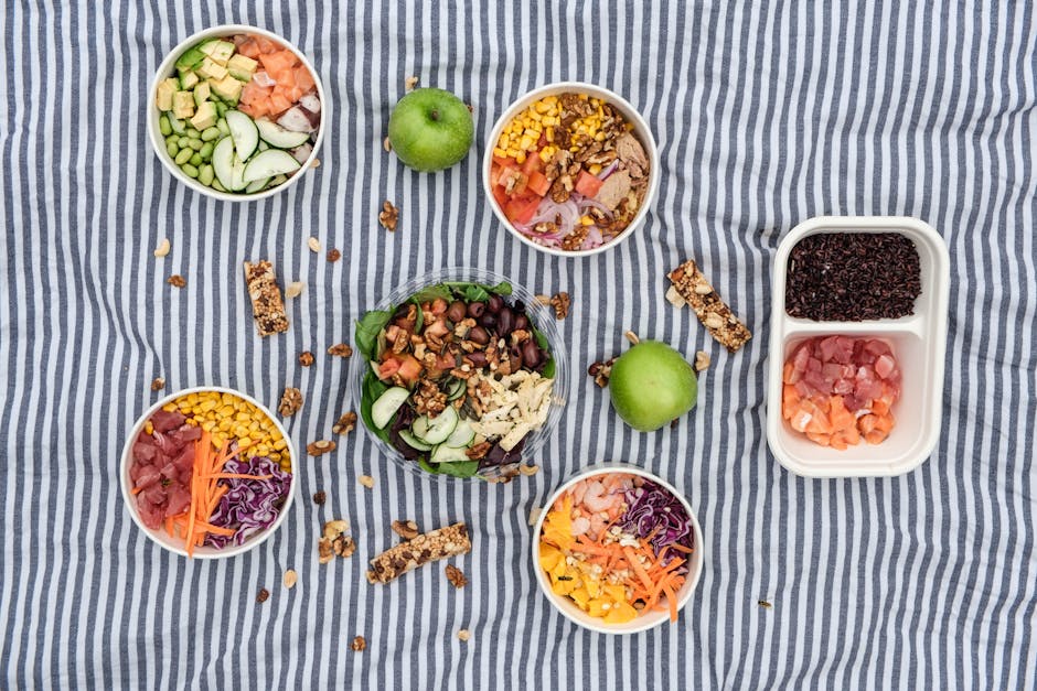 Top view of assorted healthy salad bowls on a picnic blanket with fresh ingredients.